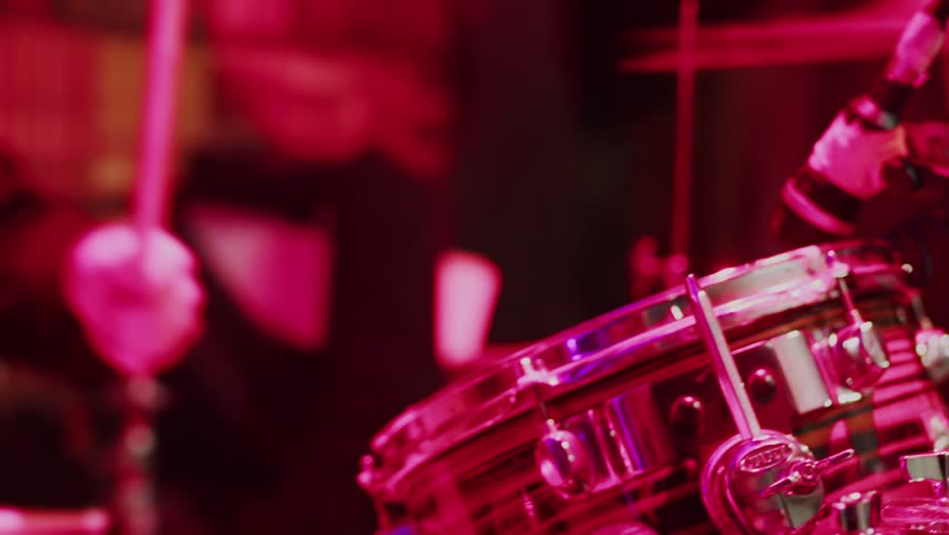 close-up of a musician playing drums passionately and quickly illuminated by pink red light, drive hi-hat from the drums, shaking from the blows of the drums Royalty-Free Stock Footage #1104911113