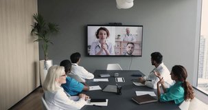 Diverse therapists in uniform take part in distant talk, engaged in group video call, attend medical concilium, remote communication, listen to colleagues on TV screen in clinic boardroom. Videocall