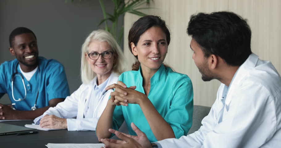 Happy diverse clinic staff take part in seminar or concilium sit at desk talking, discuss work moments, enjoy career, good teamwork results. Medical meeting event, communication of hospital workers Royalty-Free Stock Footage #1104911959