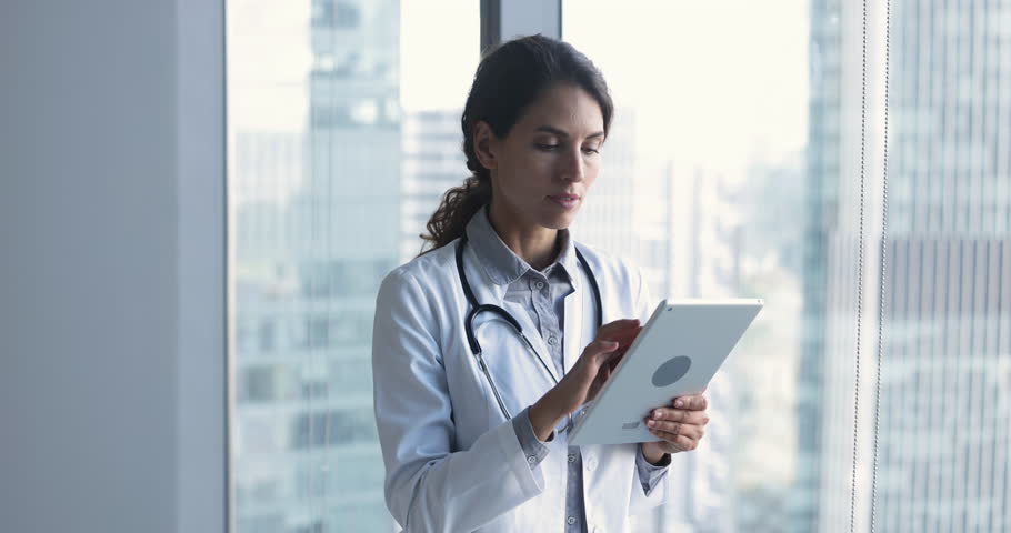 Latina physician in white uniform hold digital tablet provide remotely e-services to client, busy in on-line counselling, learn new medical application at workplace, Healthcare, technology, telehealth Royalty-Free Stock Footage #1104911967