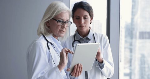 Women therapists, colleagues in white uniform with stethoscope on shoulder engaged in teamwork, discuss in hospital office use digital tablet app modern healthcare tech, review patient medical history Video de stock