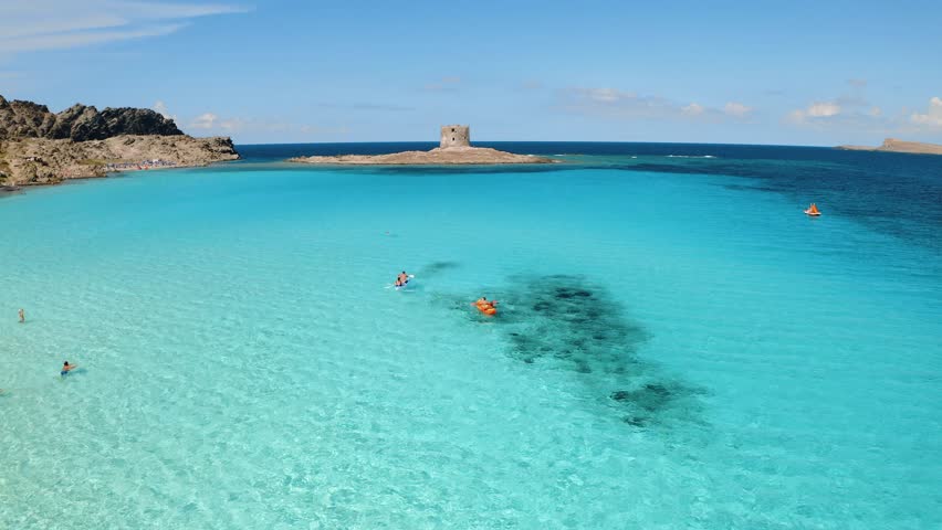 Aerial view of people on kayak and canoe in blue sea and old tower at summer sunny day. Clear azure water. La Pelosa beach, Sardinia island, Italy. Tropical. Sup boards. Active travel. Top drone view