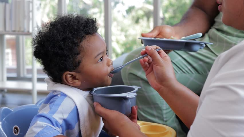Mixed race little boy happily eating food fed by mother. Mixed race family concept. baby growth. African American Royalty-Free Stock Footage #1104914221