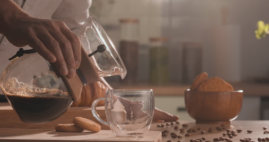 Pouring black filter coffee in cup. Barista pouring drip brewing, filtered coffee in cup with coffee beans and natural steam smoke of coffee on wooden table, slow motion Royalty-Free Stock Footage #1104917811