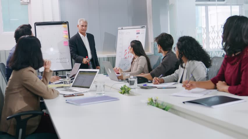 An Indian Asian senior male corporate executive businessman giving a presentation in an office meeting to diverse team of colleagues in a start up business using white board to show graphs and charts Royalty-Free Stock Footage #1104920341