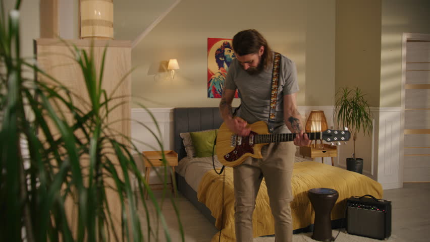 Man plays guitar in bedroom. Camera changing view to young boy playing drum set and young girl playing ukulele, jumping on bed. View of two apartments separated by wall. Concept of neighborhood.