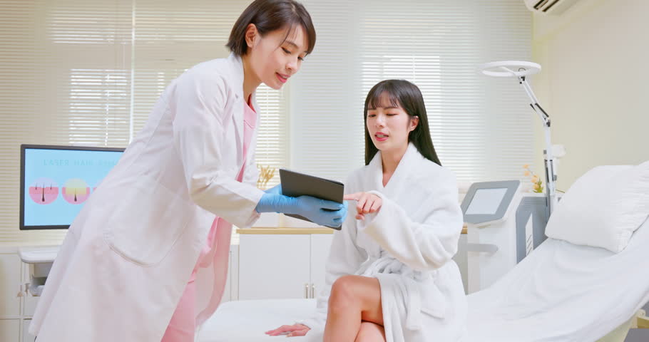 Asian female cosmetologist holding digital tablet is introducing about laser and esthetic depilation treatment at clinic when woman want to remove hair | Shutterstock HD Video #1104927319