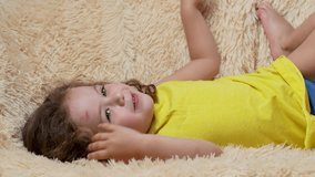 Cute little curly baby with green eyes having fun. Funny curly baby girl lying on sofa, close-up