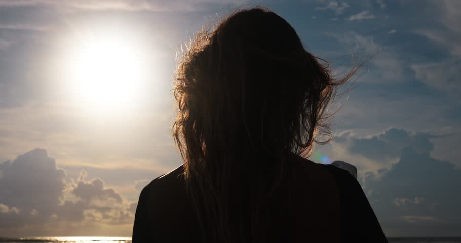 Silhouette rear view of woman with surfboard in windy weather. Hair of female surfer develops in wind giving sense of freedom, lightness. Concept of freedom and easy attitude to life without worries