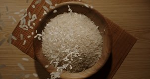 Falling Rice wooden bowl cup. Top view slow motion zoom in 4K footage. Pouring rice grains 4K video on a dark background. Asian Japanese Indian ethnicities culture healthy food. Still life relax