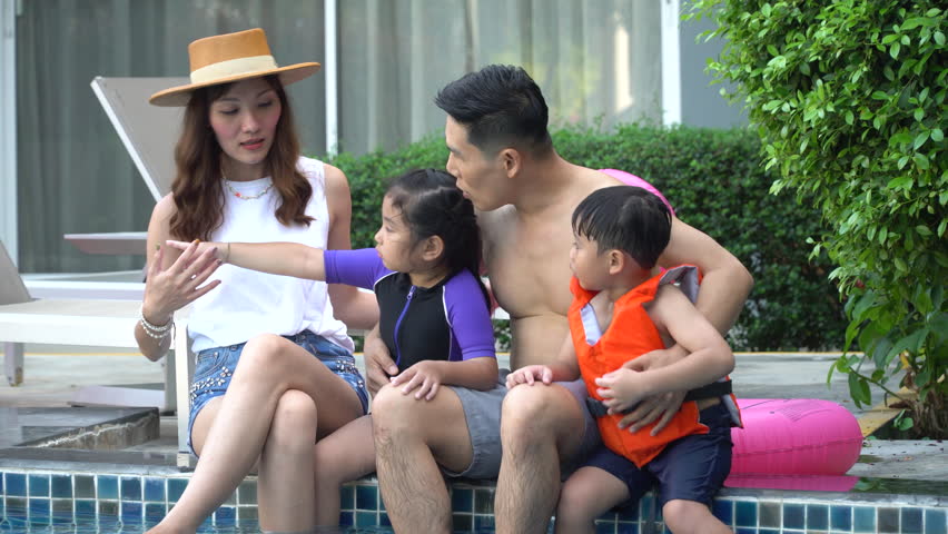 Happy asian family with inflatable or life jacket playing in swimming pool at hotel enjoying summer vacation. young father and mother daughter and son relaxing in swimming pool together outdoors
