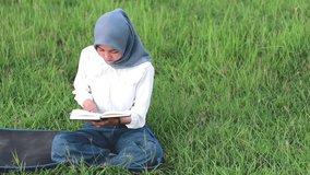 video with the concept of the activity of a young Muslim reading a book outdoors. video with the concept of the activity of a young woman wearing a hijab reading a book while sitting relaxed outdoors.