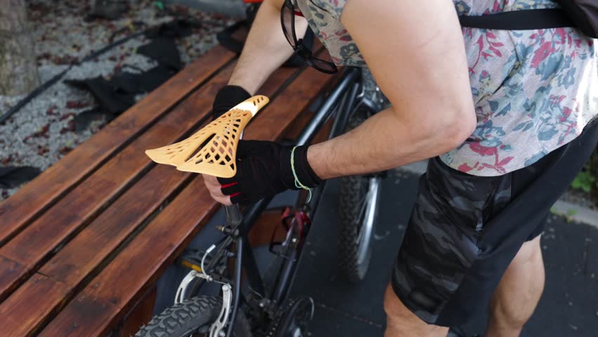 A man in gloves unscrews the bolts using a hex wrench on a mountain bike frame, fixing a bicycle seat. Urgent repair of a vehicle by a repairman on a road in a summer forest. Active lifestyle, sport.