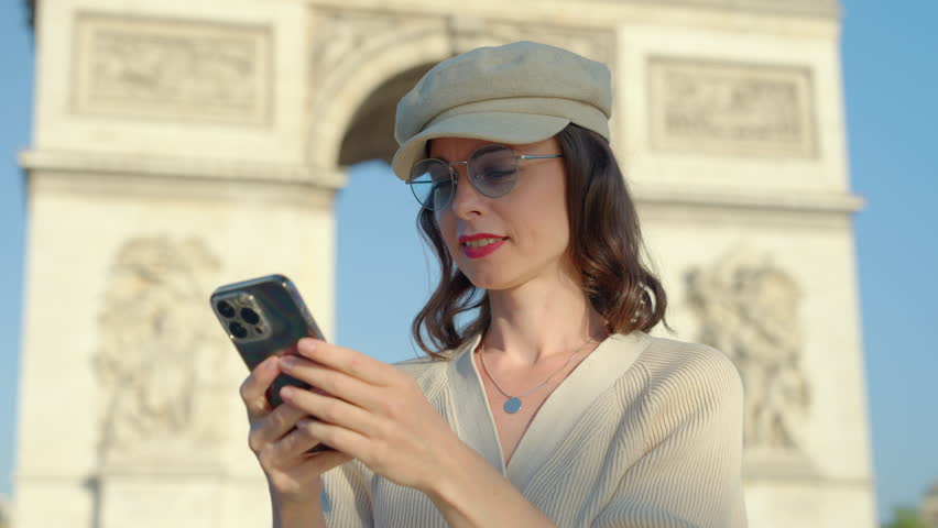 Young girl in a cap chatting with a smartphone on the background of the Arc de Triomphe Royalty-Free Stock Footage #1104946789