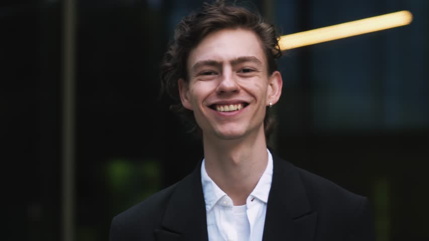 Close Up Portrait of a Happy Young Adult Male with Curly Hair and Brown Eyes Posing for Camera. Handsome Multiethnic Caucasian Male in a Suit Charmingly Smiling. Warm 