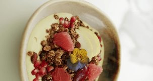 Bowl Full of Crunchy Granola Cereals with grapefruit, pomegranate, nuts, yellow hibiscus and yogurt rotating in Slow Motion. Tasty Muesli cereal. Close up. Vertical video for stories.
