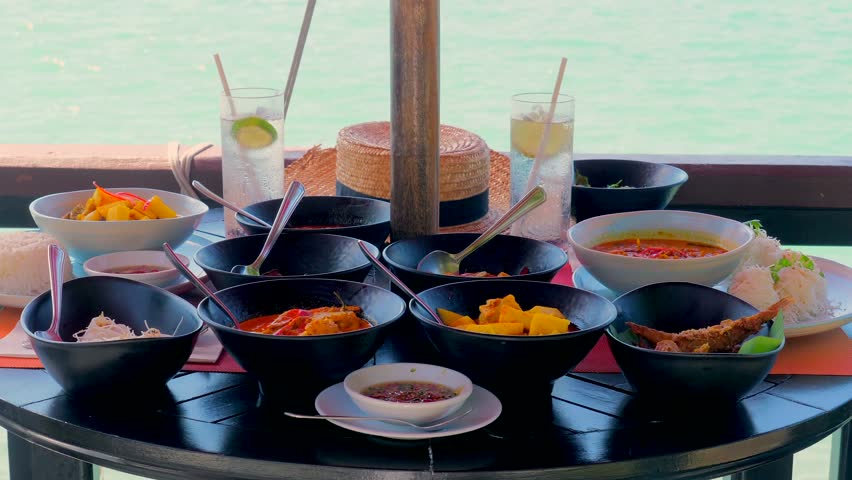 Traditional Thai food in a sea restaurant - plates filled with spicy meals like curry, fish, Tom Yum soup. Delicious Asian feast in an outdoor cafe or beachfront resort. Summer vacation in Thailand.