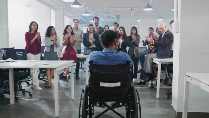 A work achievement of an Indian Asian male handicapped or physically disabled man sitting in a wheelchair applauded by a group of happy office colleagues or team members in a modern corporate start up Royalty-Free Stock Footage #1104952159
