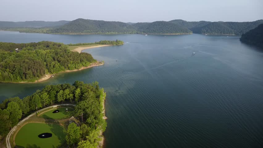 Stationary view towards Cave Run lake and Daniel Boone national forest in northeast Kentucky during sunny evening. Waves and boats on the water surface.