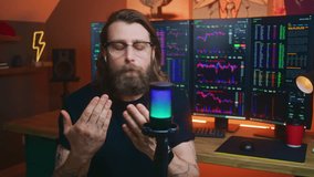 Irritated stock trader gestures, speaks aggressively on camera using microphone, records video about investment or cryptocurrency. Multi-monitor computer with real-time stocks, exchange market charts.