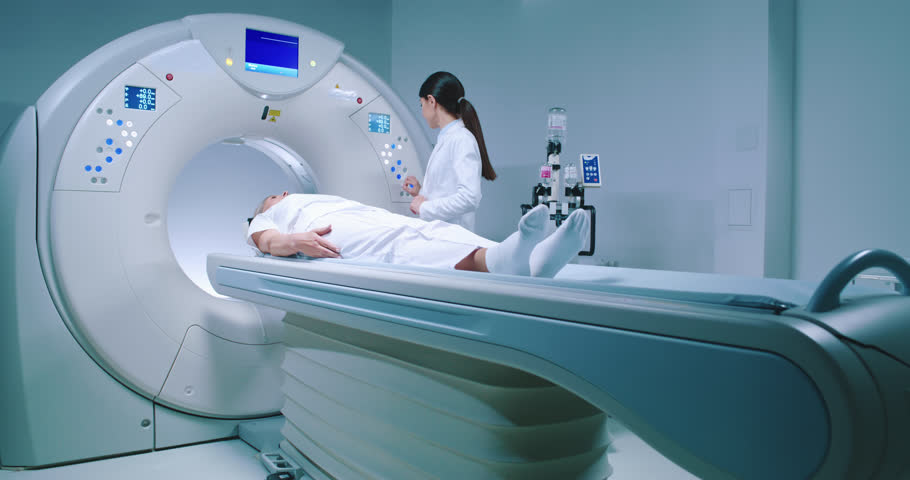 Medical worker adjusts capsule of MRI examination. Patient lies on MRI table and undergoes magnetic resonance imaging. Man in robe and protective cap enters capsule for examination. Royalty-Free Stock Footage #1104958211