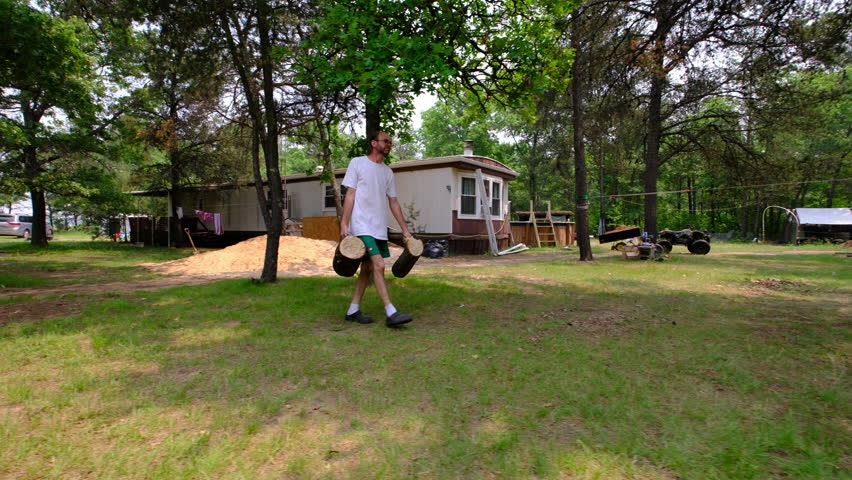 Slow motion of man carrying two logs or stumps toward his fire pit in the back yard.