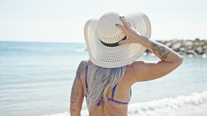 Middle age grey-haired woman tourist smiling confident wearing bikini at beach