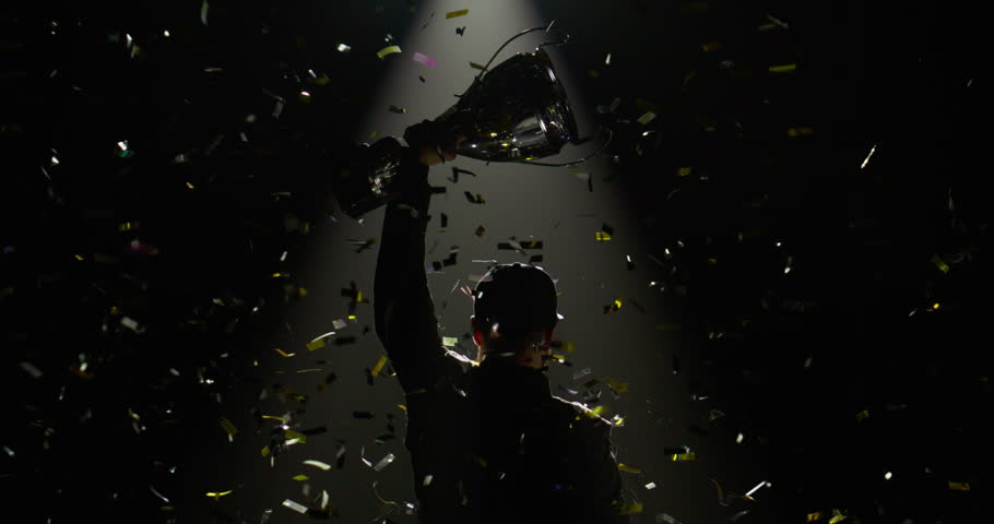 Silhouette of race car driver celebrating the win in a race against bright stadium lights, rising a trophy over his head Royalty-Free Stock Footage #1104968433