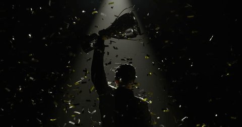 Silhouette of race car driver celebrating the win in a race against bright stadium lights, rising a trophy over his head 库存视频