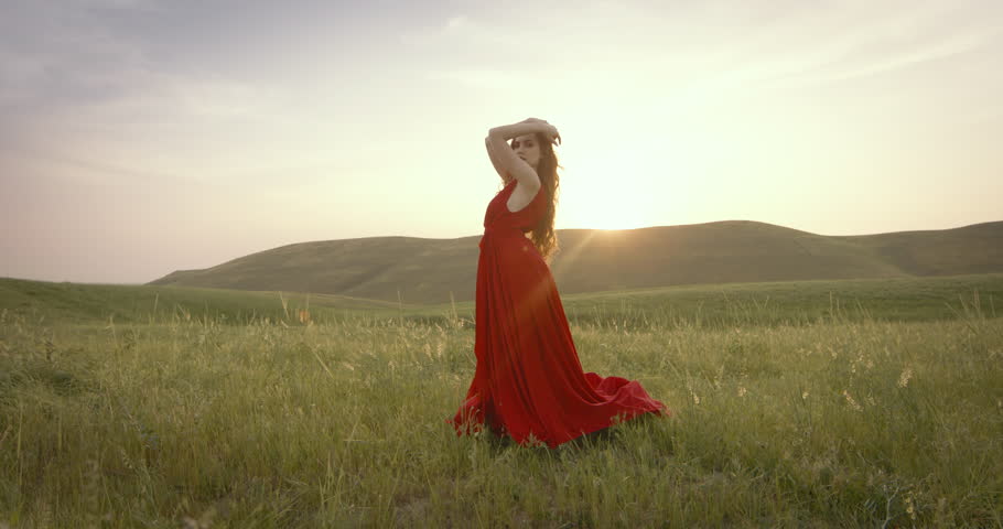 Graceful inspired woman in long fairy-tale dress posing at dawn in green field. Inspired woman in fabulous red dress posing at dawn. Concept of fabulousness, fairy tales, fantasy and inspiration. | Shutterstock HD Video #1104976289
