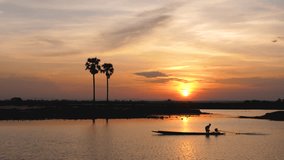 Silhouette of fisherman driving a boat on the lake. Beautiful sunset scenery with silhouette of palm trees, 4k footage