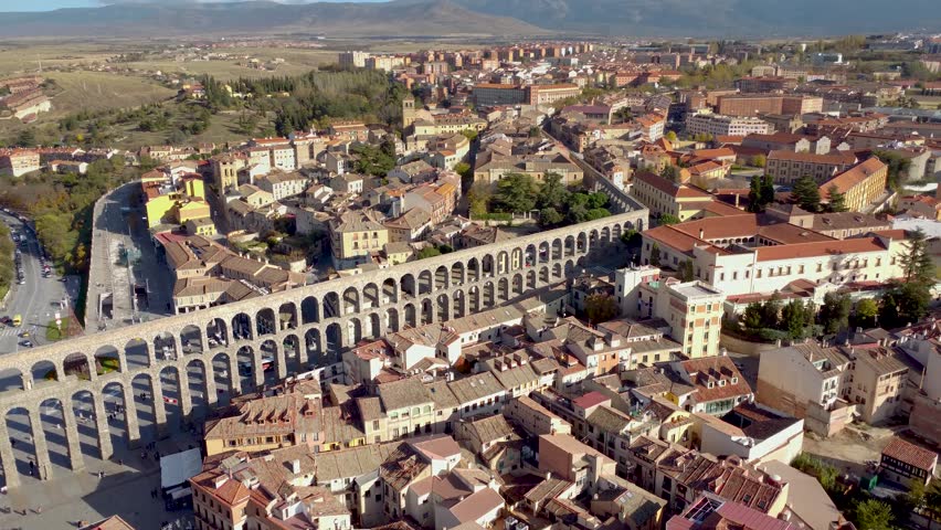 Cinematic aerial perspective of city center of Segovia. Aerial cinematic perspective of downtown Segovia. View of the ancient and famous aqueduct of Segovia, Drone backward ascending. Rooftops view Royalty-Free Stock Footage #1104983117