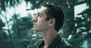 Side view of pensive male 30 years old gets wet in the rain outdoors. Cinematic video portrait of pensive male millennial in shirt standing under heavy rain outside in slow motion. Drama shot concept