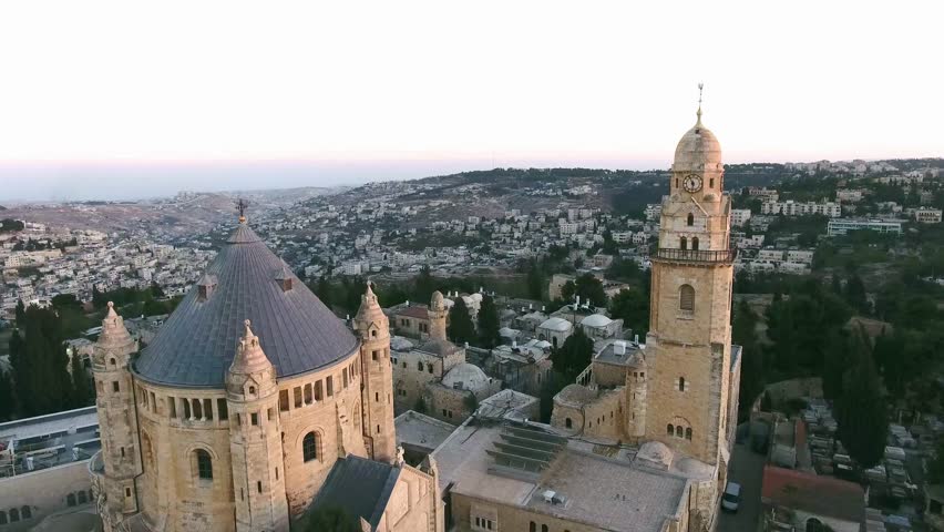 Clock tower with a cross and a metal figurine of a cockerel on a spire on Mount Zion in Jerusalem. Near the fortress is a Catholic monastery. Around the ancient buildings of yellow stone 