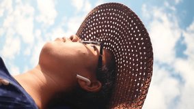 Vertical video of woman wearing a wicker hat and taking an earphone off on sunny day