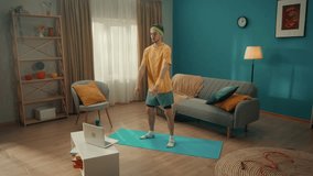 Young man doing situps on a gym mat in the living room. A man watches a video lesson on a laptop and repeats the exercises. Home fitness concept, online sports class. Slow motion.