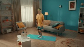Young man doing star jumps on a gym mat in the living room. A man watches a video lesson on a laptop and repeats the exercises. Home fitness concept, online sports class. Slow motion.