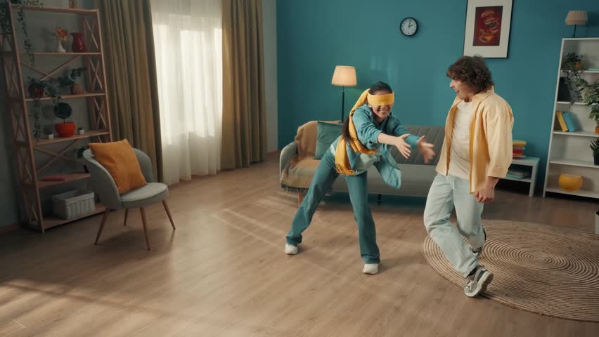 A young married couple spends time together, having fun. A couple is playing a game of blind man's buff. A blindfolded Asian woman catches a man dodging her. Family relax and entertainment at home.