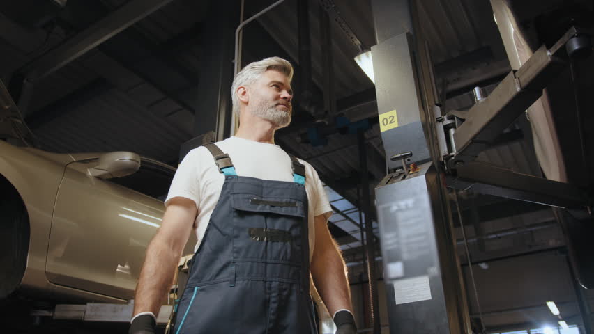 Car service station. Middle age grey haired mechanic man or smith repairing car at workshop. Professional Mechanic with wrench in garage. Pleased grey haired american car technician in the workplace