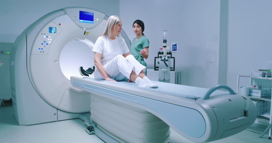 Patient is getting recommendations from doctor before MRI procedure. Woman is lying down at CT scanner bed. Female is moving into MRI scanner capsule. Female doctor is conducting tomography examining. Royalty-Free Stock Footage #1104996405