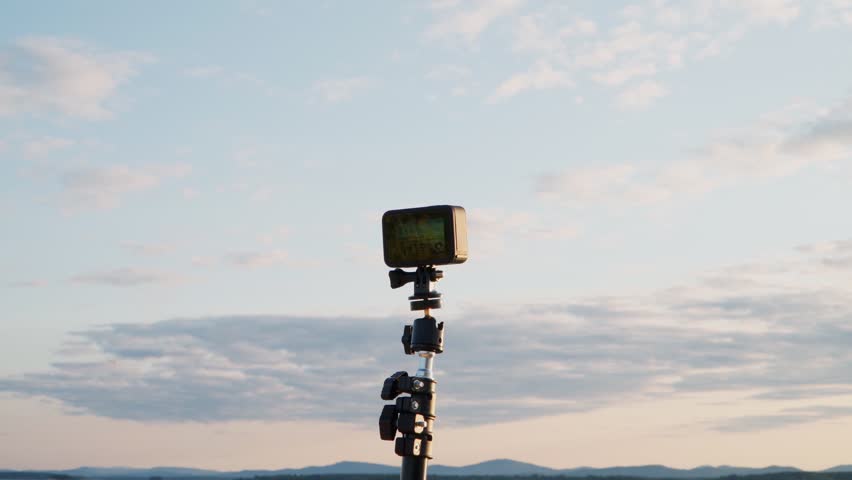 An action camera takes a time lapse of clouds and the sun on the shore of the lake.