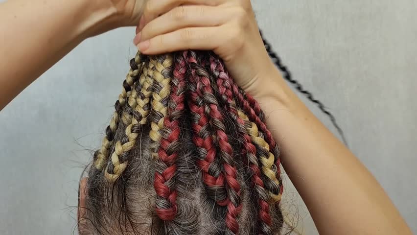 A woman gathers thin braids into a ponytail at the top of her head. Close-up video without a face. Hairstyle, dreadlocks. Gray hair, colored kanekalon.