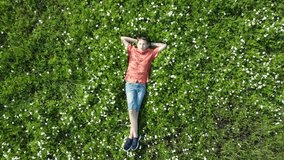 Teen boy lay and relax the green grass, blossom meadow on park. Aerial dron view.High quality 4k footage. Summer concept