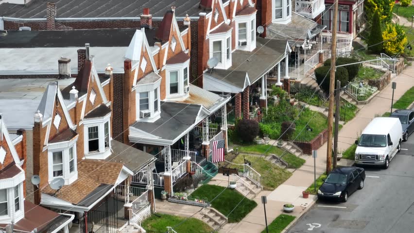 Rundown row houses with American flag on porch. Dangerous, low income urban neighborhood in USA. Long aerial zoom establishing shot.