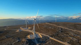 Renewable Energy in Action - Windmills on Sunset Hills Harnessing the Power of Wind, Embracing Green and Sustainable Future, Mountains and Snow in the Background, Inspiring Video Footage