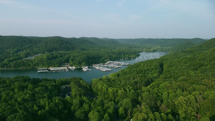Cave Run Lake bay secluded between rolling hills of Daniel Boone national forest hosting a marina with recreational boats of different sizes docked and anchored on dedicated spaces