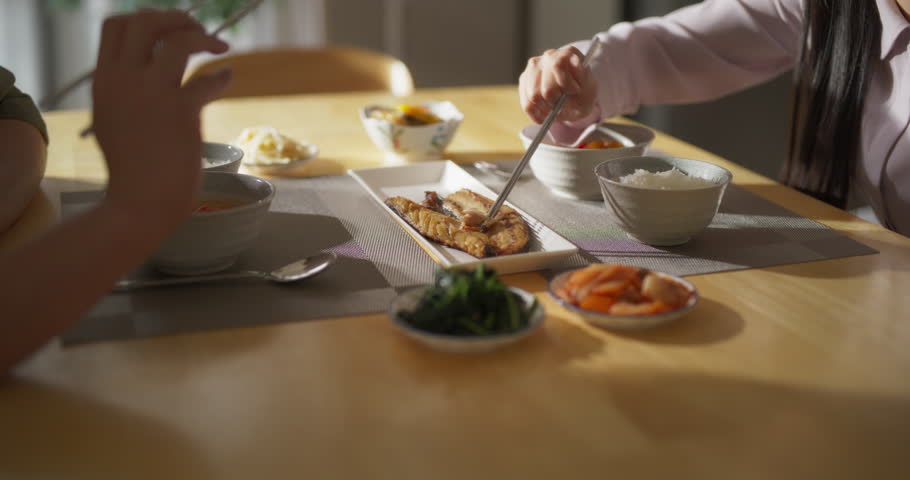 Close Up Footage Focusing on Tasty Dishes on a Dining Table with Rice Bowls, Spicy Asian Soup, Fish and Vegetables. Young Asian Man and Woman Having a Korean Lunch at Home in the Kitchen Royalty-Free Stock Footage #1105013715