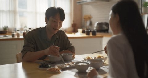 Young Loving South Korean Couple Eating Homemade Tasty Food at Home and Having a Fun Chat. Asian Boyfriend and Girlfriend Enjoying Time Together, Feasting on Cooked Fish, Spicy Vegetable Soup and Rice 스톡 비디오
