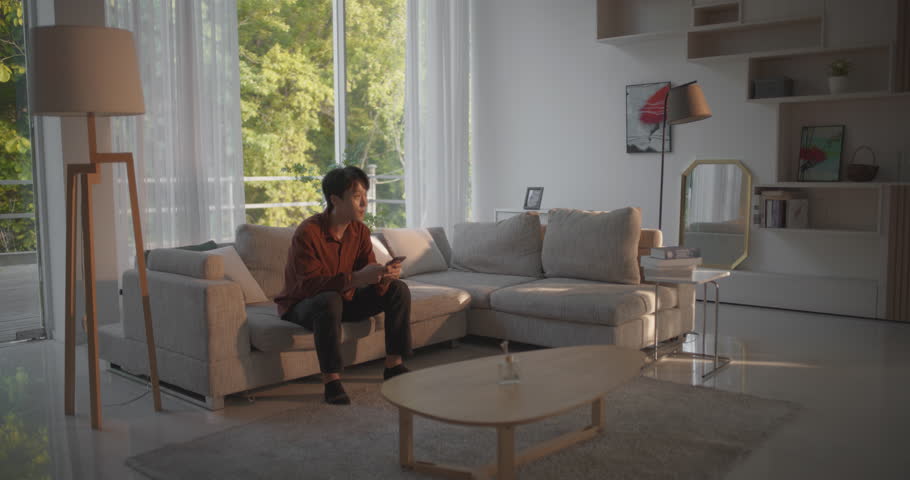 Excited South Korean Boyfriend Meeting His Girlfriend After a Long Trip. Happy Asian Couple Reunite, Hug Each Other at Home Spin and Fall Down on a Comfortable Sofa in a Stylish Living Room Royalty-Free Stock Footage #1105013723