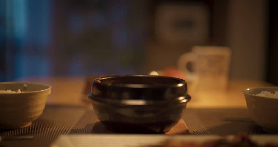 Close Up of a Couple Eating Delicious Korean Dinner with Chopsticks in the Kitchen at Home. Footage Focusing on Food on the Dining Table with Rice Bowls, Asian Soup and Spicy Asian Meat